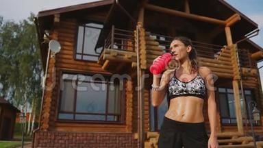 运动的女人，在一个木制豪宅的背景下，一个漂亮的压在黑色顶部的美女，锻炼了饮用水